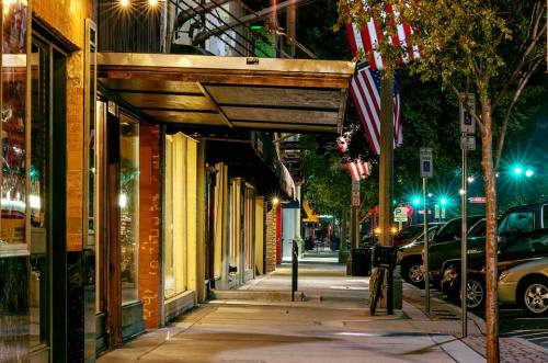 A quiet street at night with storefronts, American flags, and parked cars under soft street lighting.