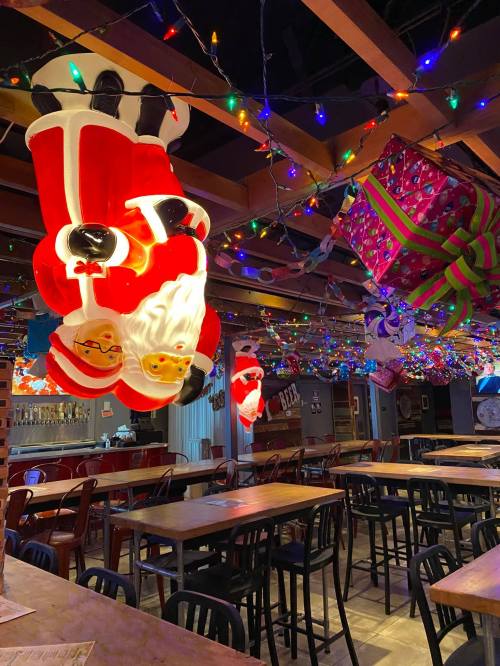 A festive indoor space decorated with hanging Santa figures and colorful string lights, with tables arranged below.