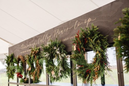A display of festive wreaths hanging on a wall under a tent, with elegant handwritten signage above.