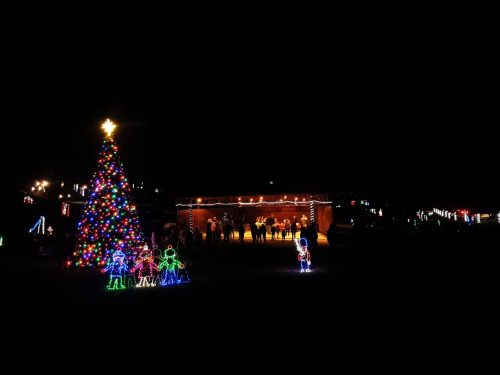 A brightly lit Christmas tree and colorful decorations illuminate a festive gathering at night.