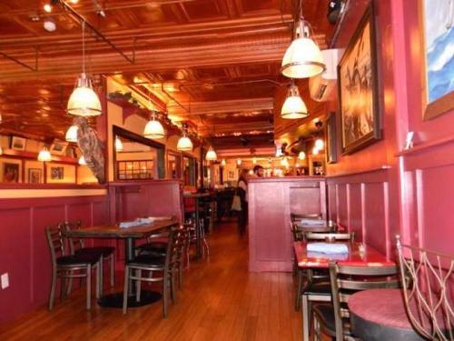 Cozy restaurant interior with wooden floors, red walls, and warm lighting, featuring tables and artwork on the walls.