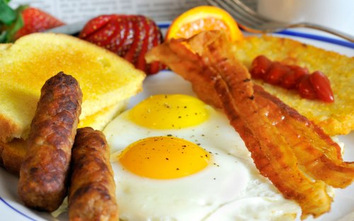A hearty breakfast plate with two sunny-side-up eggs, bacon, sausage, toast, hash browns, and fresh fruit.