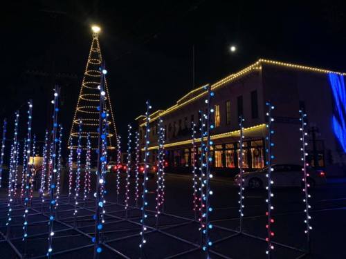 A festive scene at night featuring a lit Christmas tree and colorful lights in front of a building.
