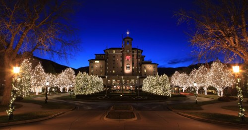 A grand hotel illuminated with festive lights, surrounded by trees, against a twilight sky.