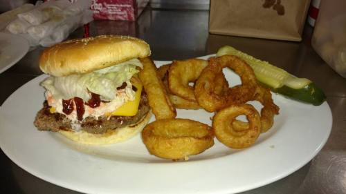 A cheeseburger with lettuce, sauce, and a pickle, served with crispy onion rings on a white plate.