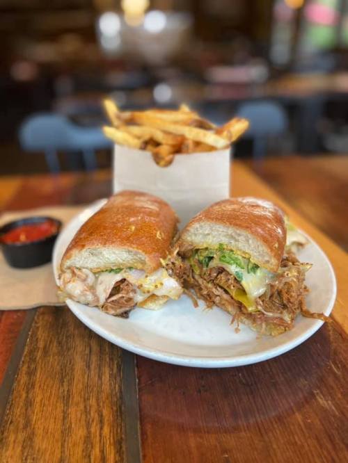 A plate with two sandwiches filled with meat and greens, accompanied by a side of fries and a small cup of dipping sauce.