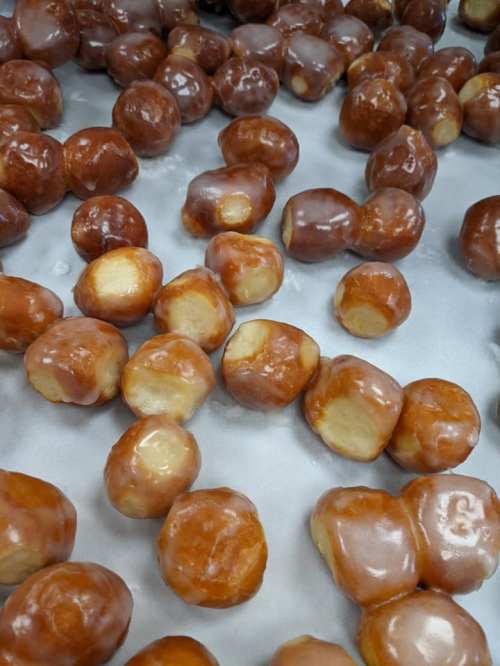 A close-up of glazed doughnut holes scattered on a surface, showcasing their shiny brown exterior.