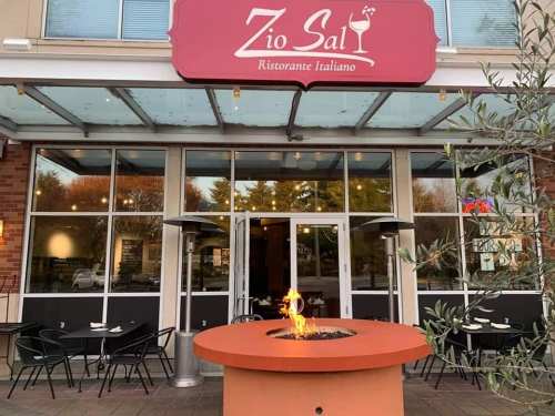 Exterior of Zio Sal, an Italian restaurant, featuring a fire pit and outdoor seating under a glass canopy.