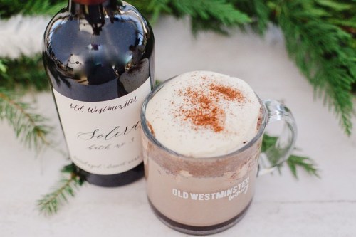 A glass of creamy hot chocolate topped with whipped cream and nutmeg, next to a bottle of Old Westminster wine.