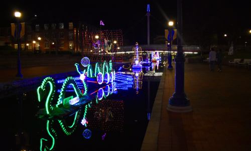 Colorful lights reflect on a calm waterway at night, showcasing festive decorations along the banks.