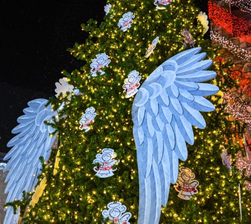 A decorated Christmas tree with blue angel wings and festive lights, surrounded by snowflakes.
