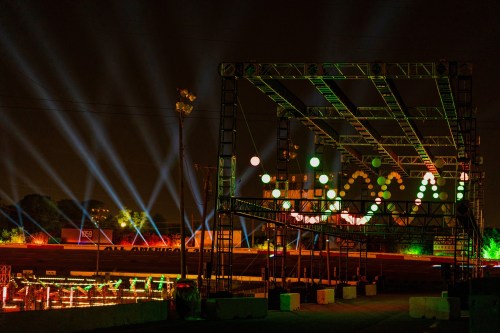 A vibrant night scene of a racetrack with colorful lights and a large stage structure illuminated by beams.