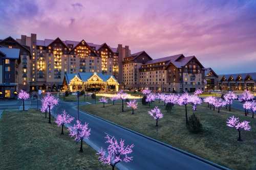 A beautifully lit hotel at dusk, surrounded by glowing pink trees and a colorful sky.