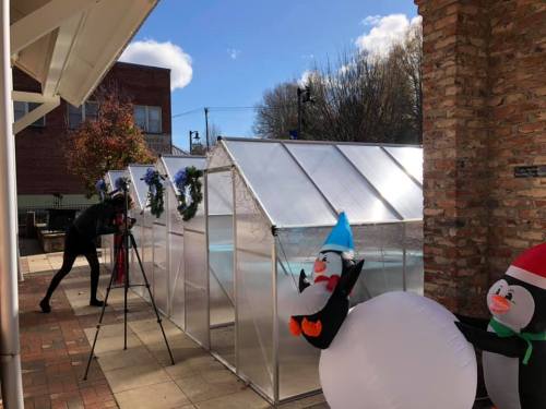 A photographer captures a festive scene with greenhouses and inflatable snowmen decorated for the holidays.