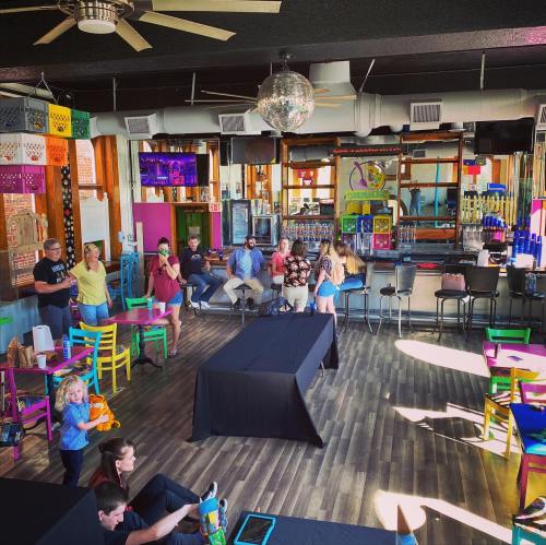 A colorful indoor space with people socializing, tables, and a disco ball, creating a lively atmosphere.