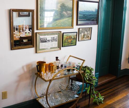 A stylish bar cart with glassware and bottles, set against a gallery wall of framed art and photographs.