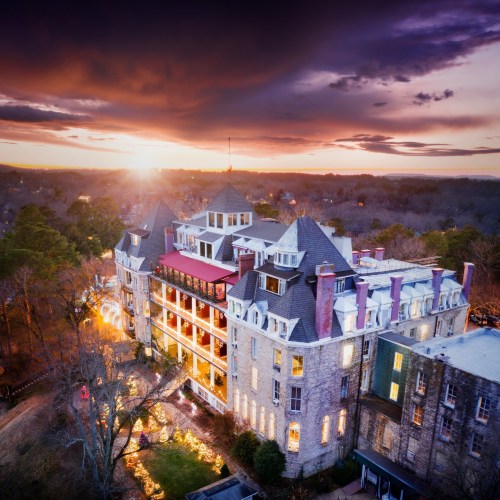 A historic hotel at sunset, with dramatic clouds and warm light illuminating its architecture and surrounding trees.