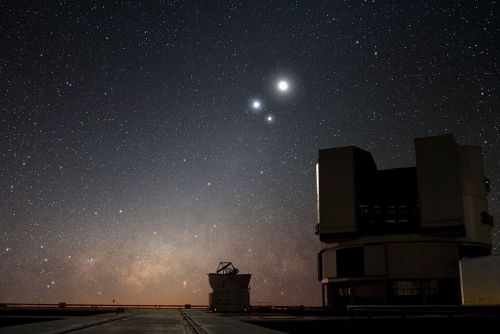 A starry night sky with two bright celestial bodies and an observatory silhouette in the foreground.