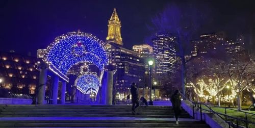 A nighttime scene of a city park adorned with blue lights, featuring a historic clock tower and festive decorations.