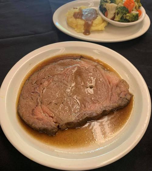 A plate of juicy roast beef in gravy, served with mashed potatoes and a side of mixed vegetables.