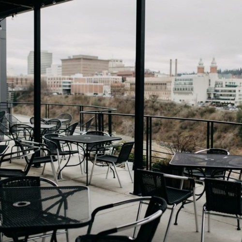 Outdoor seating area with black tables and chairs overlooking a city skyline on a cloudy day.