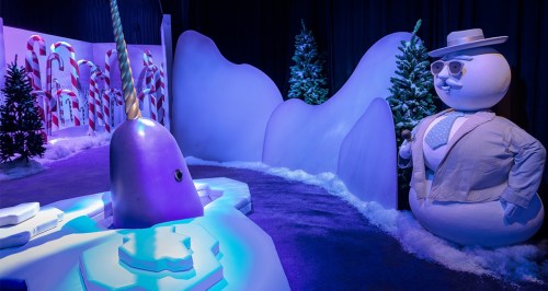 A whimsical winter scene featuring a purple narwhal and a snowman in a snowy, festive setting with candy canes.