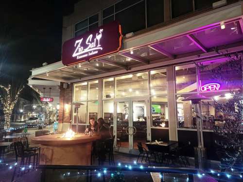 A cozy restaurant exterior at night, with a sign reading "Zio Sal," warm lighting, and outdoor seating.