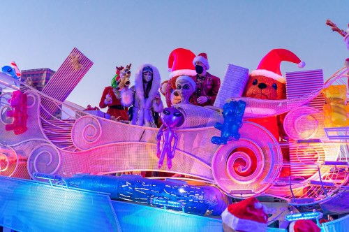 A colorful float with festive characters in Santa hats, including animals and an alien, against a bright sky.