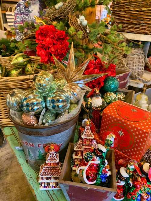 A festive display of colorful Christmas ornaments, including shiny baubles and decorative figurines, in rustic containers.