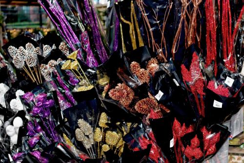 Colorful decorative floral arrangements in black packaging, featuring glittery pinecones and leaves in purple, red, and gold.