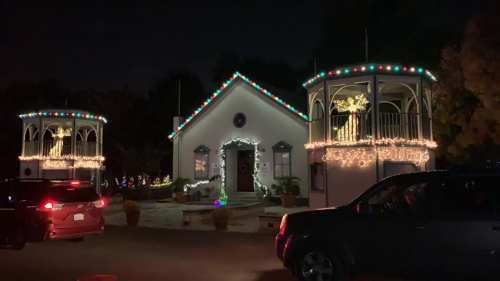 A festive house at night, adorned with colorful holiday lights and decorations on the porch and surrounding trees.
