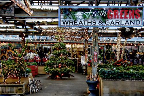 A festive market display featuring fresh greens, wreaths, and garland, adorned with lights and a decorated tree.