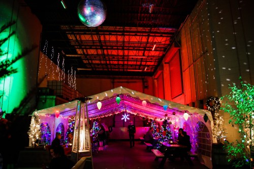 A festive indoor space decorated with colorful lights, Christmas trees, and a disco ball, creating a cheerful atmosphere.