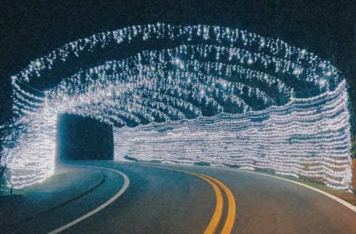 A winding road illuminated by a tunnel of bright white lights at night.