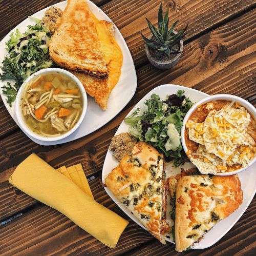 Two plates of food: one with grilled cheese, salad, and soup; the other with cheesy bread, salad, and chili with toppings.