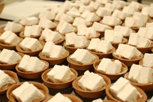 A close-up of numerous small dessert cups filled with chocolate and topped with large marshmallow squares.