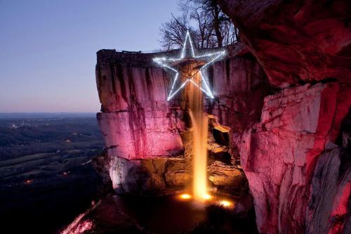 A waterfall cascades from a cliff, illuminated by colorful lights and a large star decoration above.