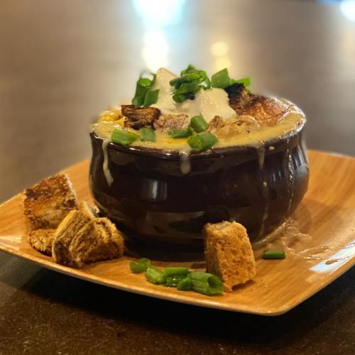 A bowl of creamy soup topped with green onions, croutons, and served on a wooden plate with bread pieces.