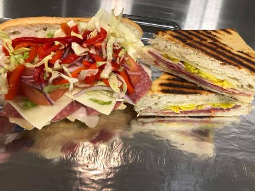 A freshly made sandwich with layers of meats, cheese, and vegetables, served alongside a grilled sandwich.