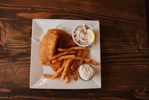 A plate of fried fish fillets, French fries, coleslaw, and a lemon wedge on a wooden table.
