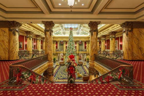 A grand lobby decorated for Christmas, featuring a tall tree, ornate columns, and festive garlands.