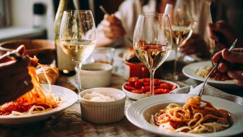 A cozy dining scene with plates of spaghetti, wine glasses, and people enjoying a meal together.