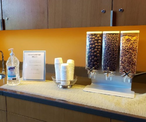A countertop with a hand sanitizer dispenser, cups, and a three-chambered dispenser filled with snacks.