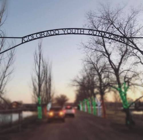 Archway reading "Colorado Youth Outdoors" with trees lit in green, set against a twilight sky.
