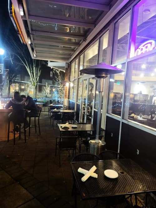 Outdoor dining area with empty tables and chairs, illuminated by string lights, in a cozy restaurant setting.