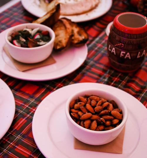 A table setting with bowls of almonds and salad, alongside bread and a decorative mug on a plaid tablecloth.