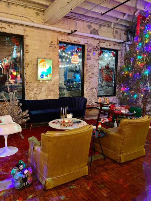 Cozy holiday scene with a decorated Christmas tree, festive decor, and seating area in a warmly lit room.
