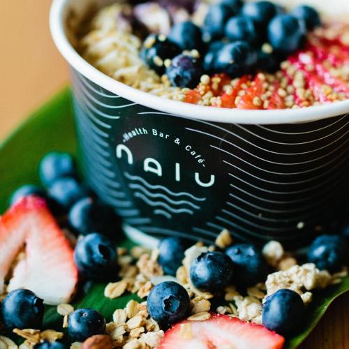 A bowl of smoothie topped with blueberries, strawberries, granola, and seeds, placed on a green leaf.