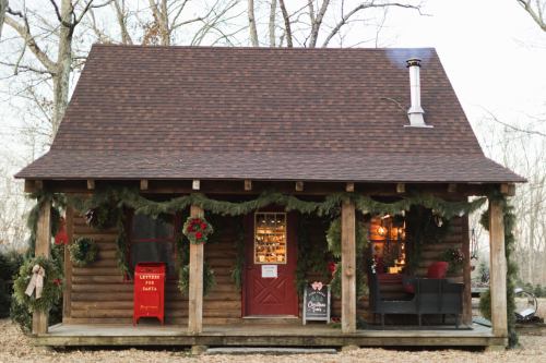 A cozy log cabin decorated for the holidays, featuring wreaths, a red mailbox, and a welcoming porch.