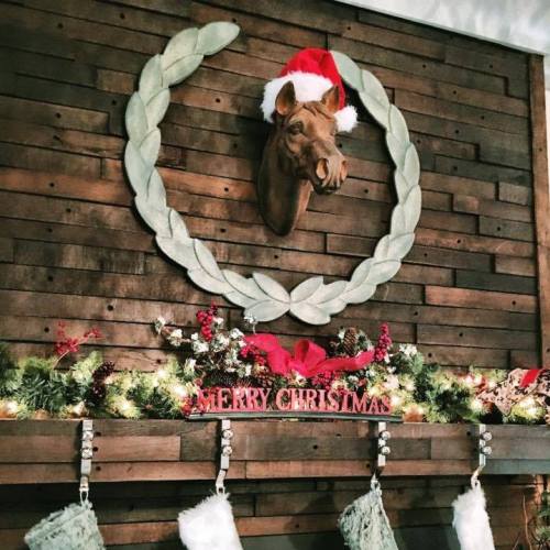 A festive wall display featuring a horse head in a wreath, Christmas stockings, and a "Merry Christmas" sign.